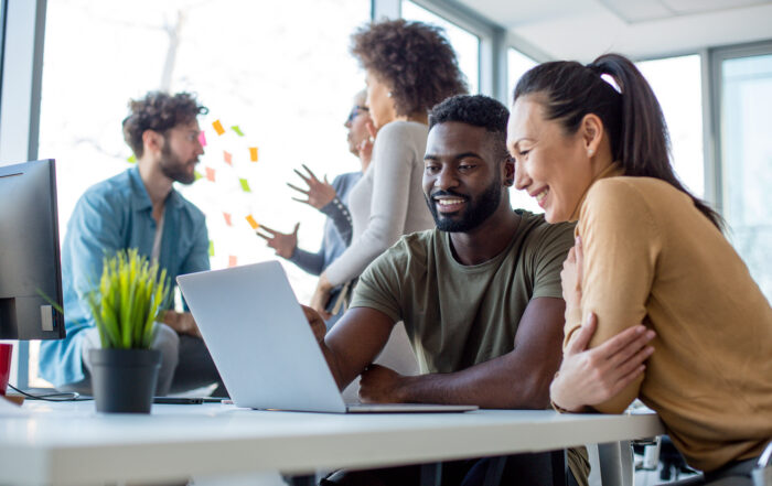 Man and woman looking at a laptop together with people in background