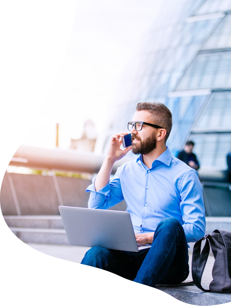 man sat outside in the sun on the phone with a laptop