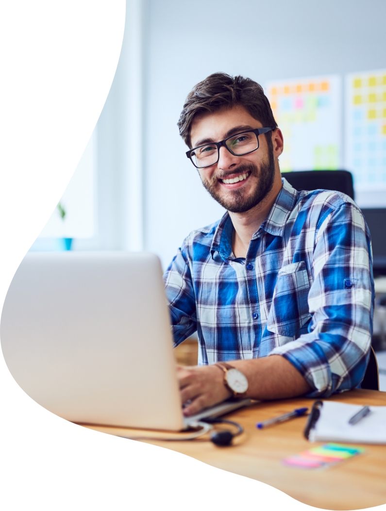 man in checkered shirt smiling whilst working on a laptop